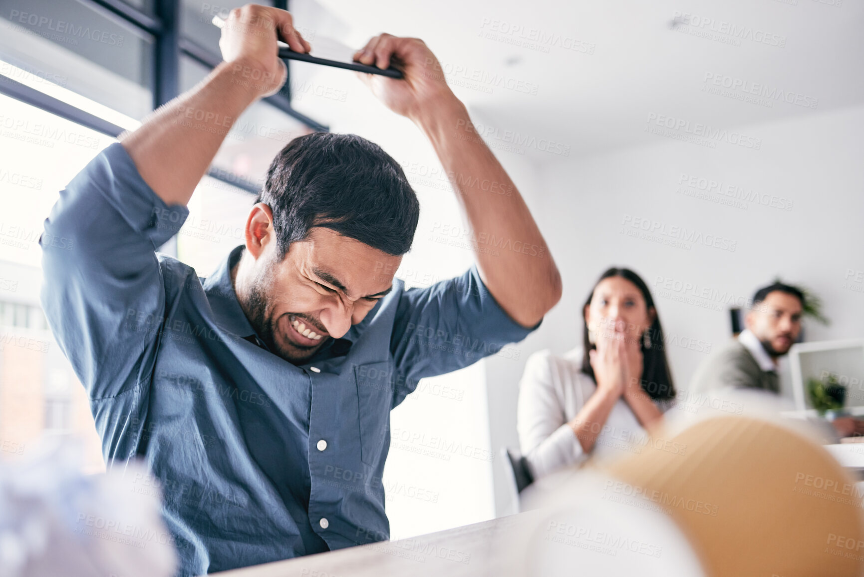 Buy stock photo Shot of a handsome young businessman sitting in the office and breaking his digital tablet in anger