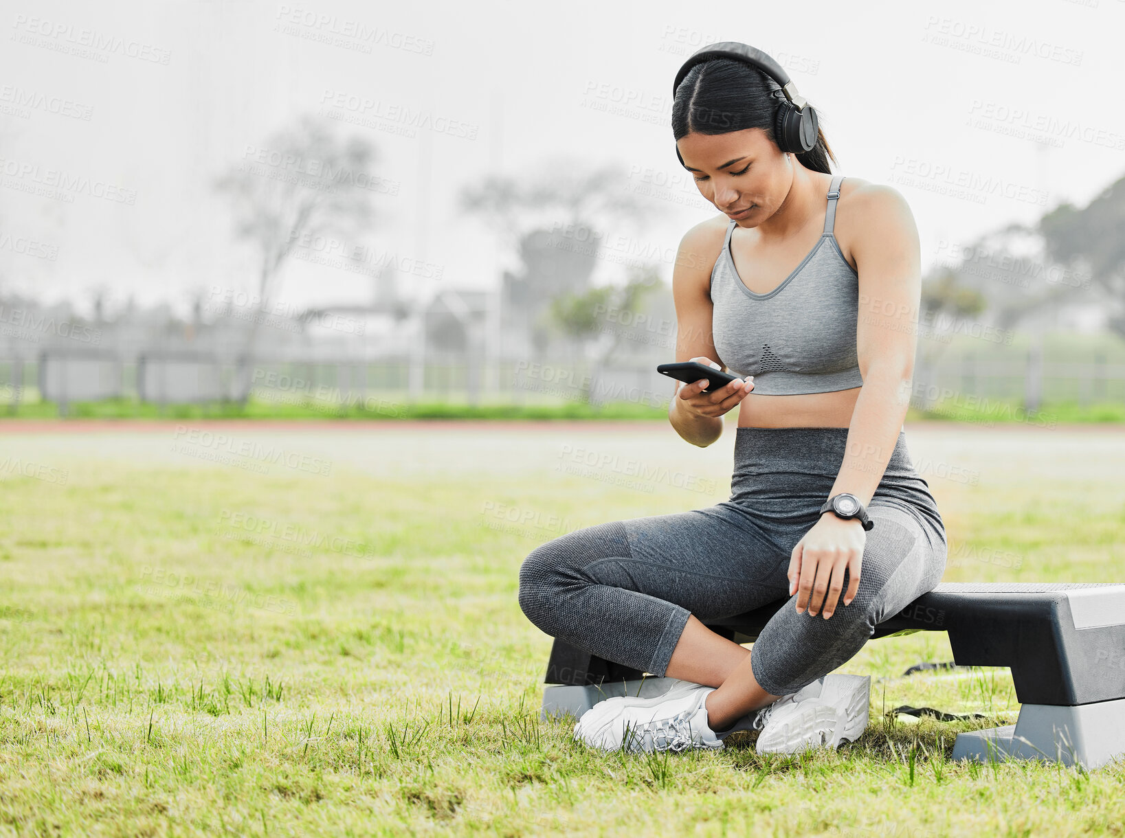 Buy stock photo Full length shot of an attractive young female athlete checking her messages while exercising outside