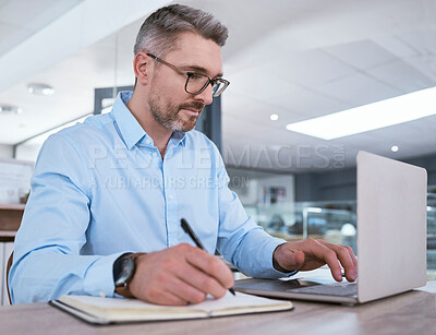 Buy stock photo Shot of a mature businessman writing notes while working on a laptop in an office