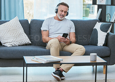 Buy stock photo Shot of a mature man listening to music using his smartphone at home