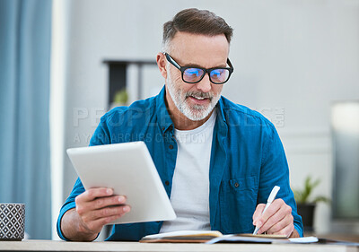 Buy stock photo Shot of a mature businessman using his digital tablet while working from home