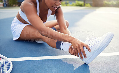 Buy stock photo Shot of an unrecognizable woman sitting alone and stretching before playing tennis