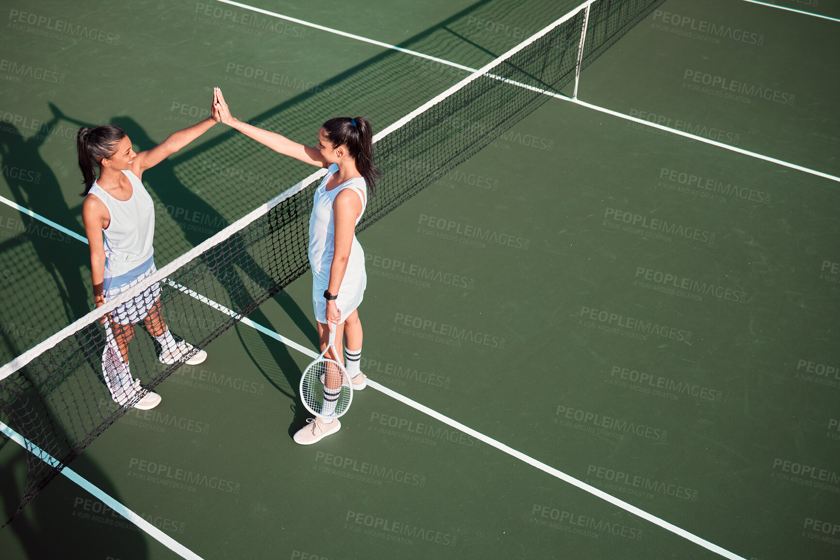 Buy stock photo Shot of two sporty young women giving each other a high five while playing tennis together on a court