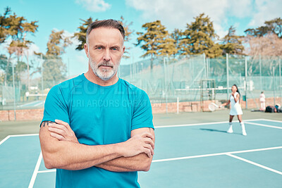 Buy stock photo Shot of a handsome mature coach standing on a tennis court with his arms crossed during practise