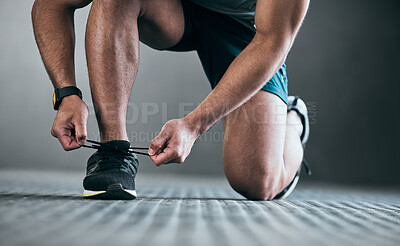 Buy stock photo Cropped shot of an unrecognizable young male athlete tying his laces against a grey background