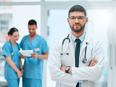Buy stock photo Shot of a young male doctor standing with his arms crossed at a hospital
