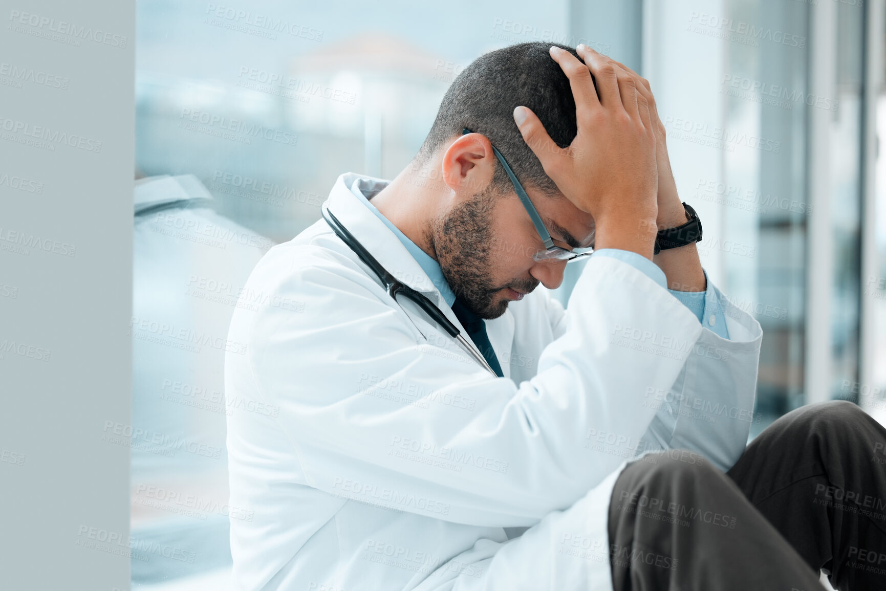 Buy stock photo Shot of a young male doctor looking stressed out while at work at a hospital
