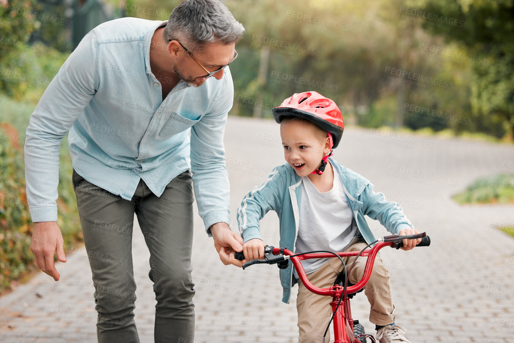 Buy stock photo Father, son and learning to bike in outdoor, parent support and training activity for kid. Dad, boy and teaching cycling outside or helping for child development, exercise and helmet for safety