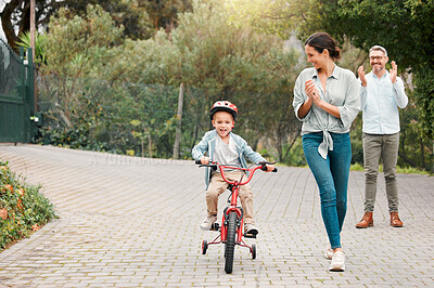 Buy stock photo Shot of a little boy wearing a helmet and riding a bike outside with his mother