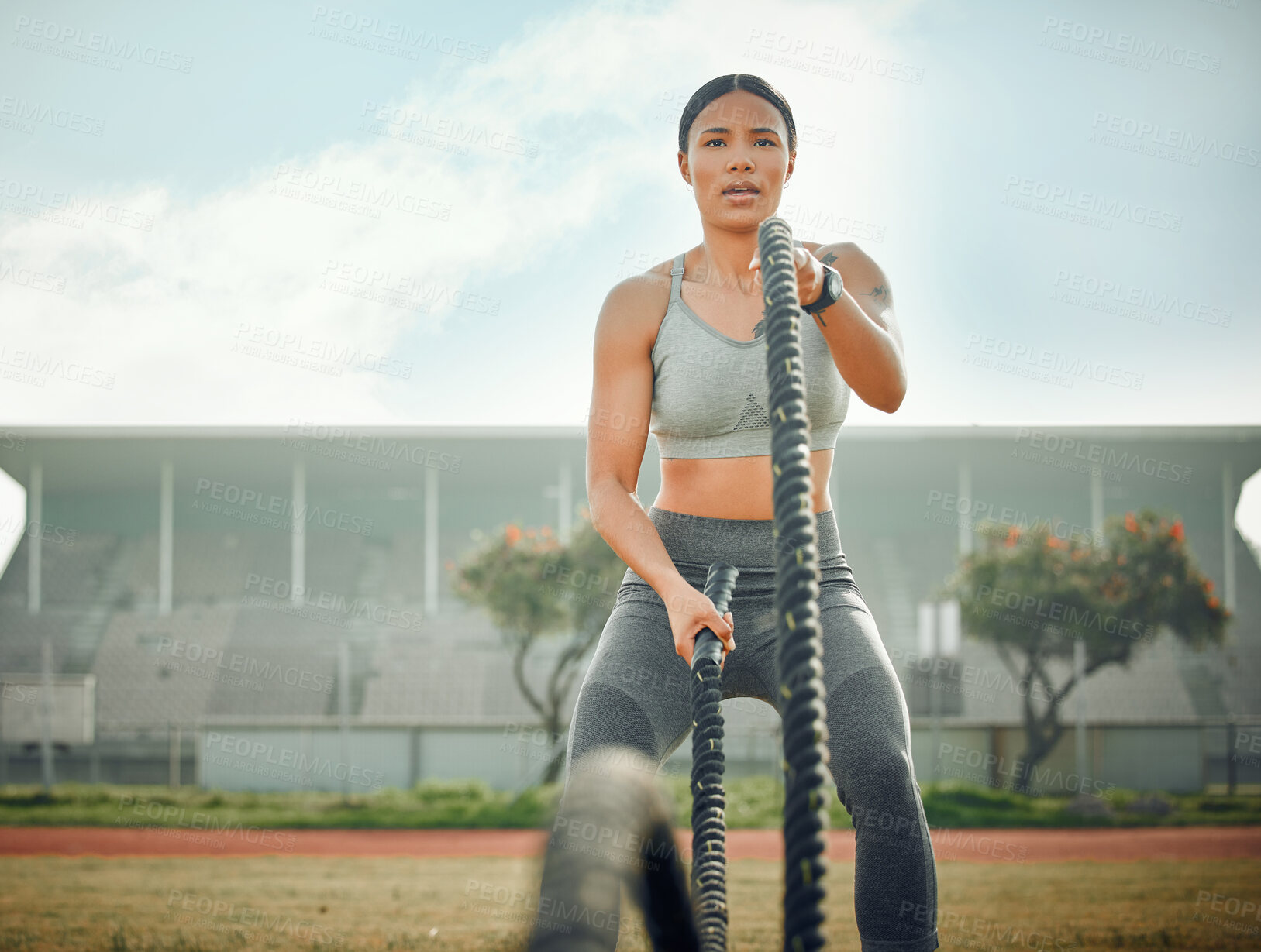 Buy stock photo Cropped shot of an attractive young female athlete exercising with battle ropes outside