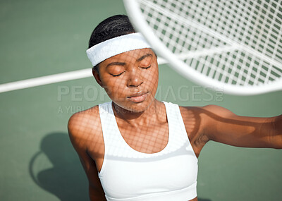 Buy stock photo Shot of a sporty young woman shielding her face from the sun with a tennis racket on a court