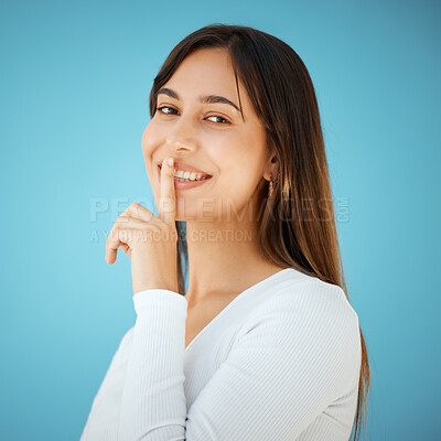 Buy stock photo Studio shot of a young woman holding her finger to her lips against a blue background