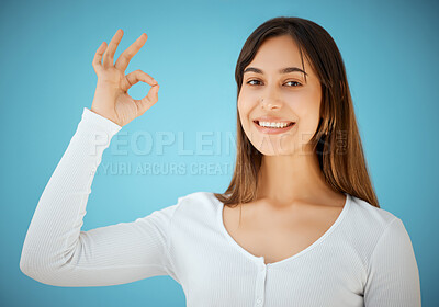 Buy stock photo Studio shot of a young woman showing an OK against a blue background