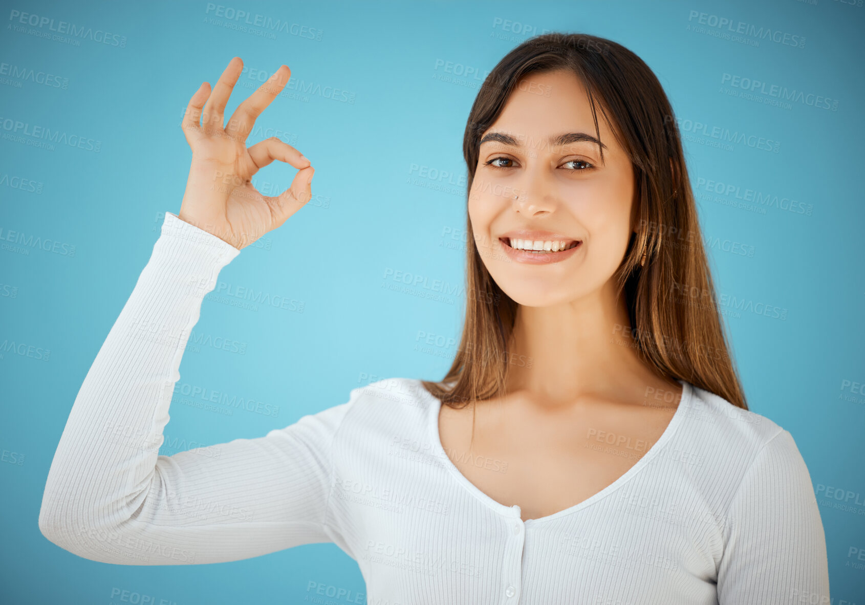 Buy stock photo Studio shot of a young woman showing an OK against a blue background