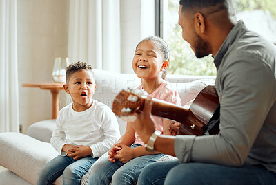 Buy stock photo Shot of a young father teaching his kids how to play the guitar while sitting on the sofa at home