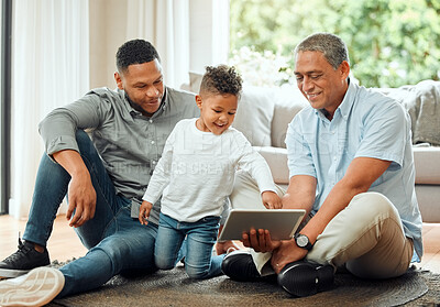 Buy stock photo Shot of an older man sitting on the floor with his son and watching his grandson use a digital tablet