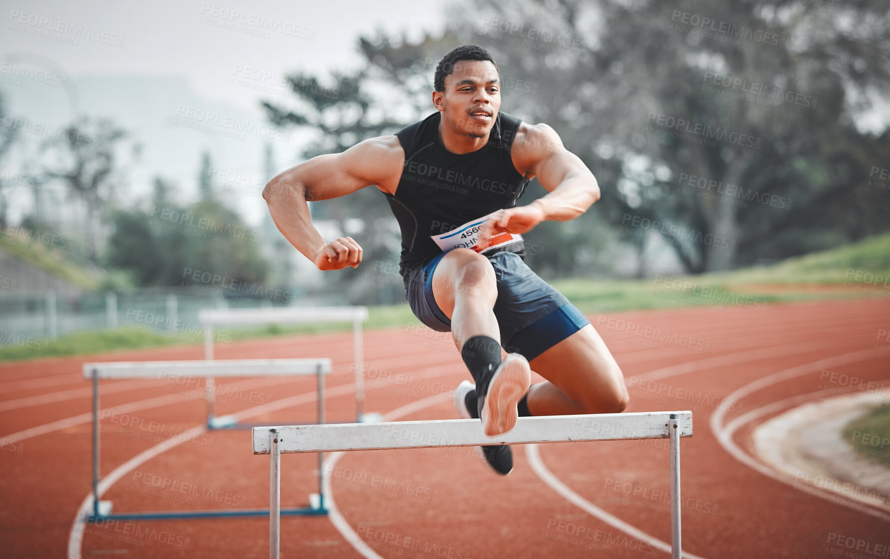 Buy stock photo Full length shot of a handsome young male athlete practicing hurdles on an outdoor track