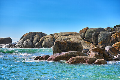 Buy stock photo Boulders or big rocks in a calm ocean against a clear blue sky background with copy space. Beautiful seascape across the horizon and rocky coast. Perfect destination for a summer holiday or getaway