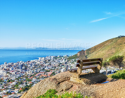 Buy stock photo Public bench on a cliff looking at the city and sea in summer. Scenic and landscape view of a seat on a mountain to relax and enjoy the view of the town. Peaceful, quiet, and secluded natural area