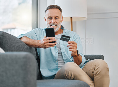 Buy stock photo Shot of a mature man sitting alone on his sofa at home and using his cellphone for online shopping