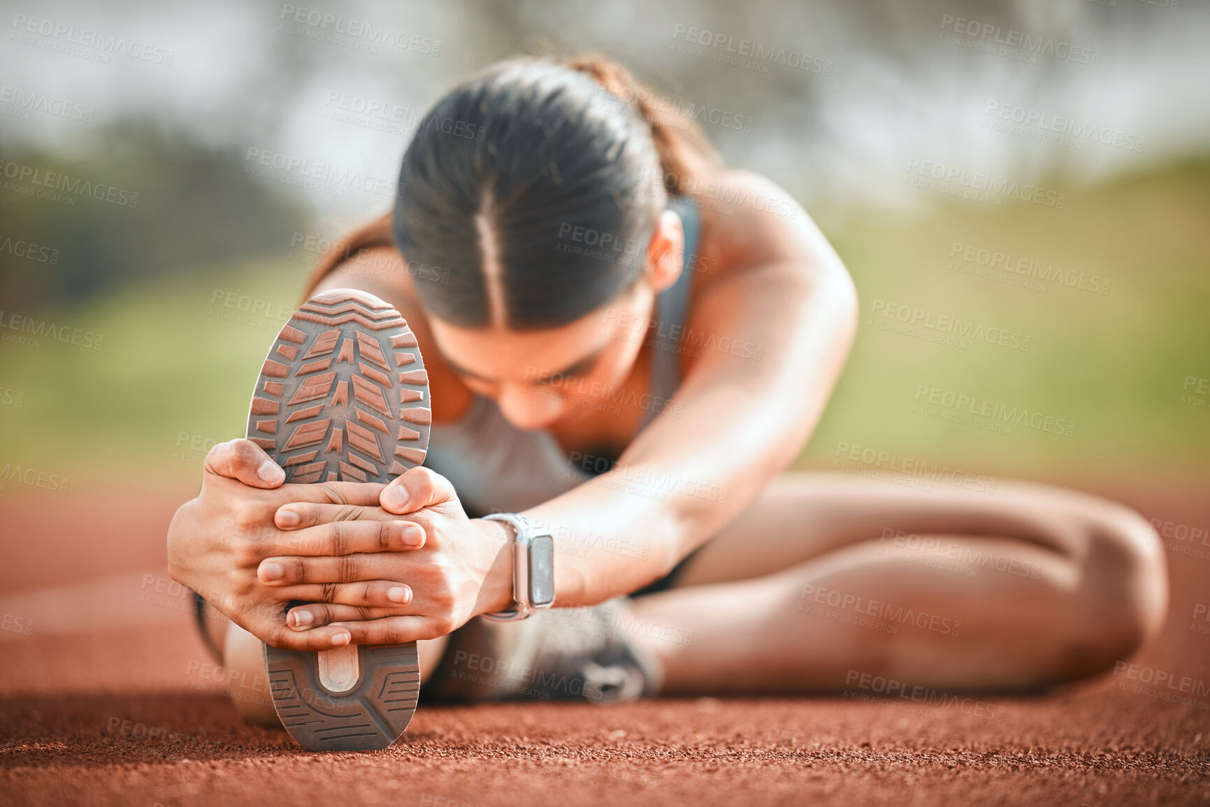 Buy stock photo Shot of a young athlete stretching her legs on a running track outdoors