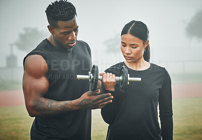 Buy stock photo Shot of a sporty young woman exercising with dumbbells with the help of a trainer outdoors