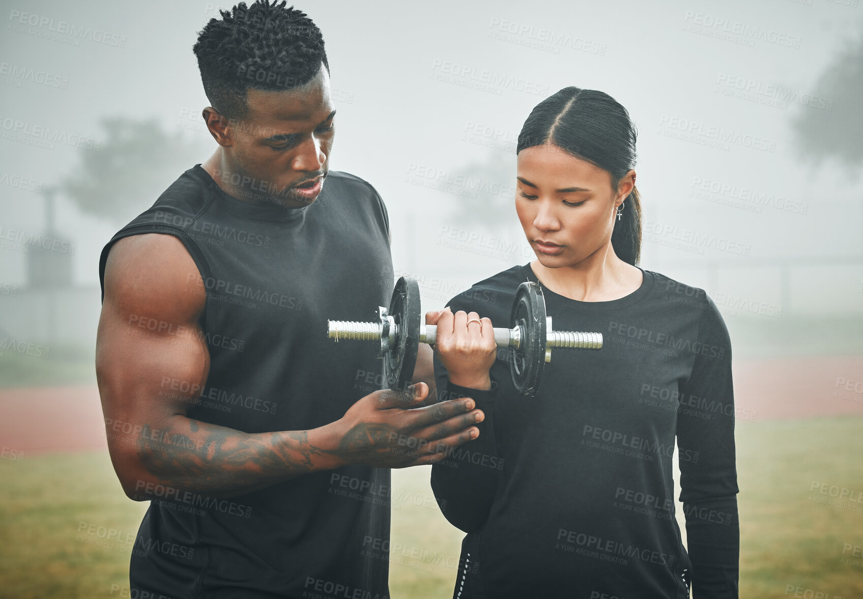 Buy stock photo Fitness, weights and personal trainer with woman in nature for arm strength, muscles and tone. Sports, fog and male instructor helping female athlete with dumbbell for lifting exercise in field. 