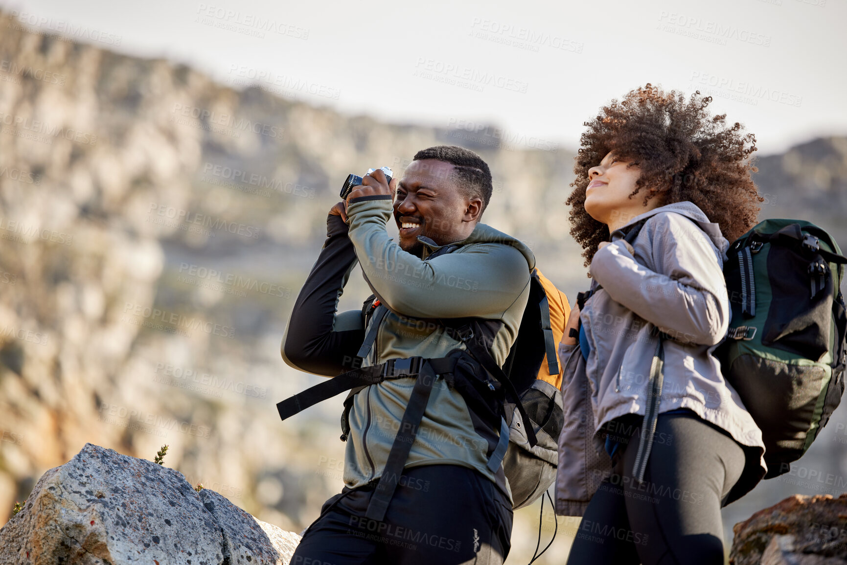 Buy stock photo Hiking, camera and photographer with couple in mountains for journey, climbing and travel. Relax, trekking and adventure with black man and woman hiker in nature for exercise, picture and motivation