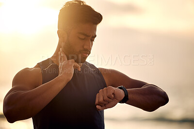 Buy stock photo Shot of a sporty young man checking his pulse while exercising outdoors