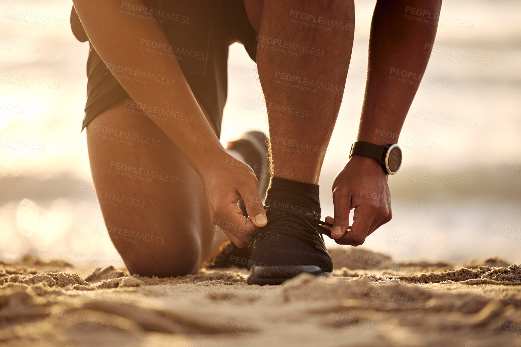 Buy stock photo Closeup shot of an unrecognisable man tying his laces while exercising at the beach