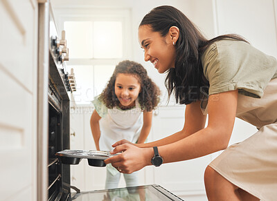 Buy stock photo Shot of a mother and daughter putting a tray of muffins into the oven