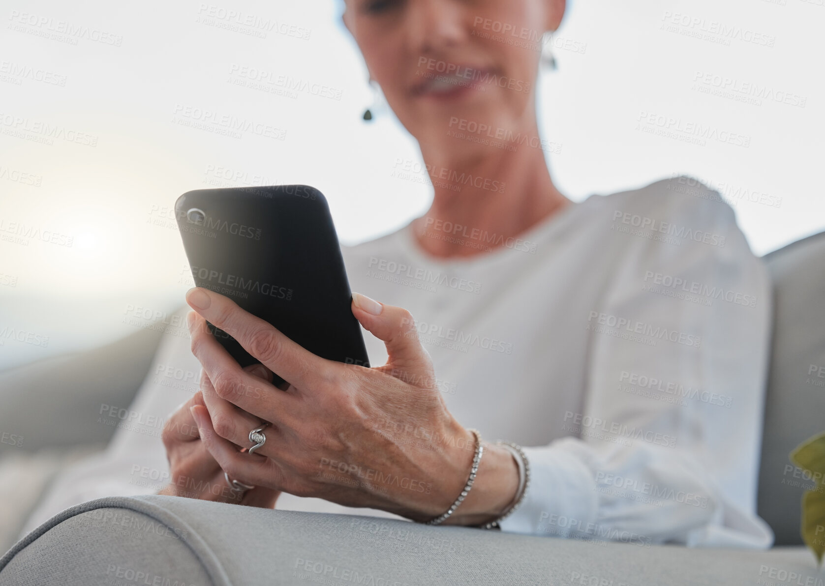 Buy stock photo Mature woman, phone and texting on sofa with hands, contact or listen in living room at house. Person, smartphone and happy with conversation, smile or social network on mobile app in apartment