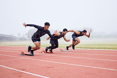 Buy stock photo Full length shot of three handsome young male athletes starting their race on a track
