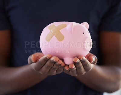 Buy stock photo Shot of an unrecognisable man holding a piggybank with a band aid over it
