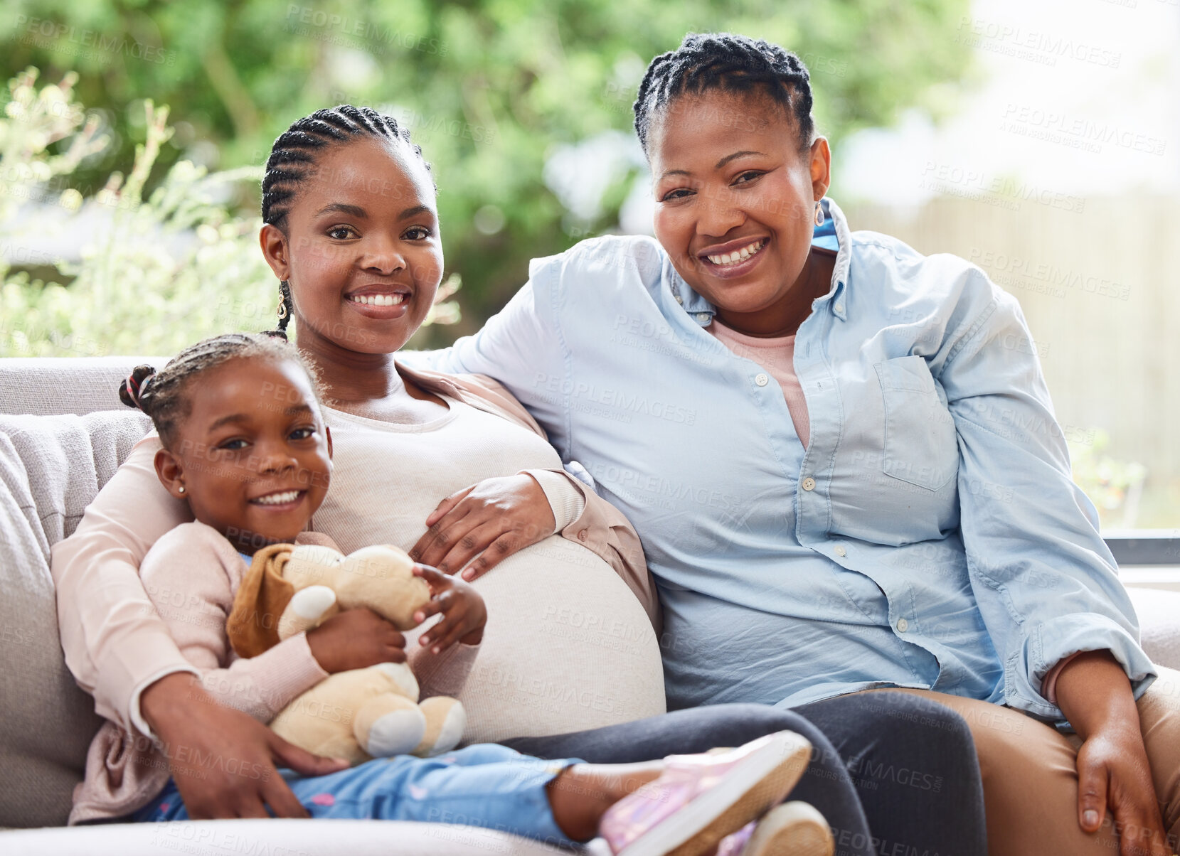 Buy stock photo Cropped portrait of an attractive young pregnant woman sitting on the sofa at home with her mother and daughter