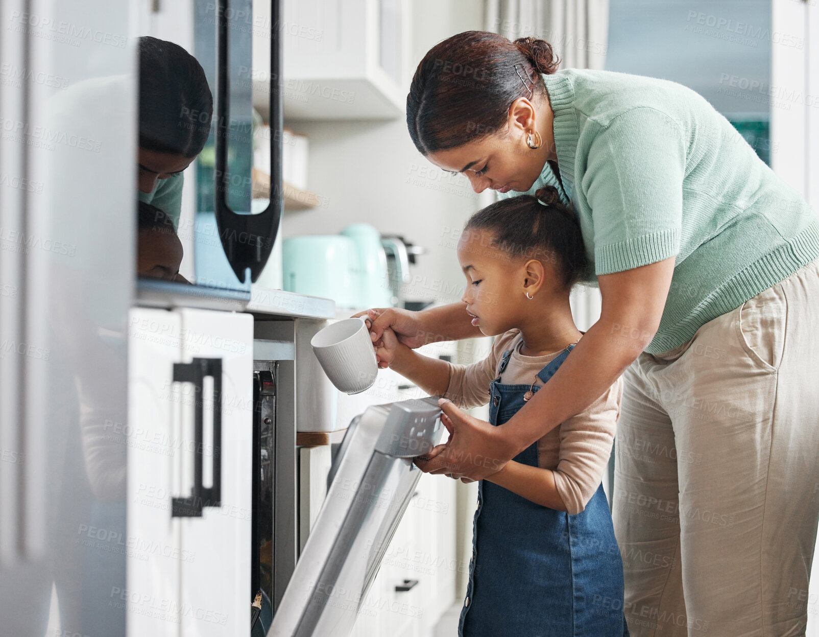 Buy stock photo Shot of a little girl putting a cup into the dishwashing machine at home with her mother