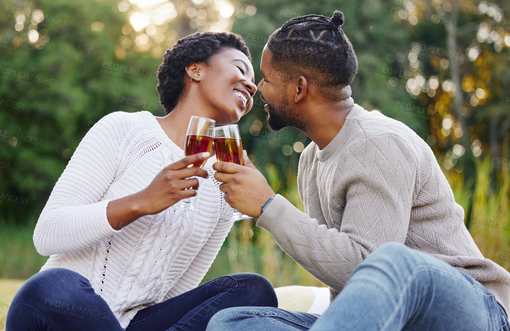 Buy stock photo Black couple, wine and picnic in nature with cheers for anniversary date, honeymoon celebration and romance with kiss. People, relax and happy on grass in park with support, success and holiday fun