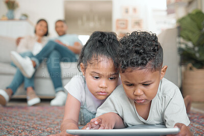 Buy stock photo Shot of two young children lying on the floor in the living room and using a digital tablet