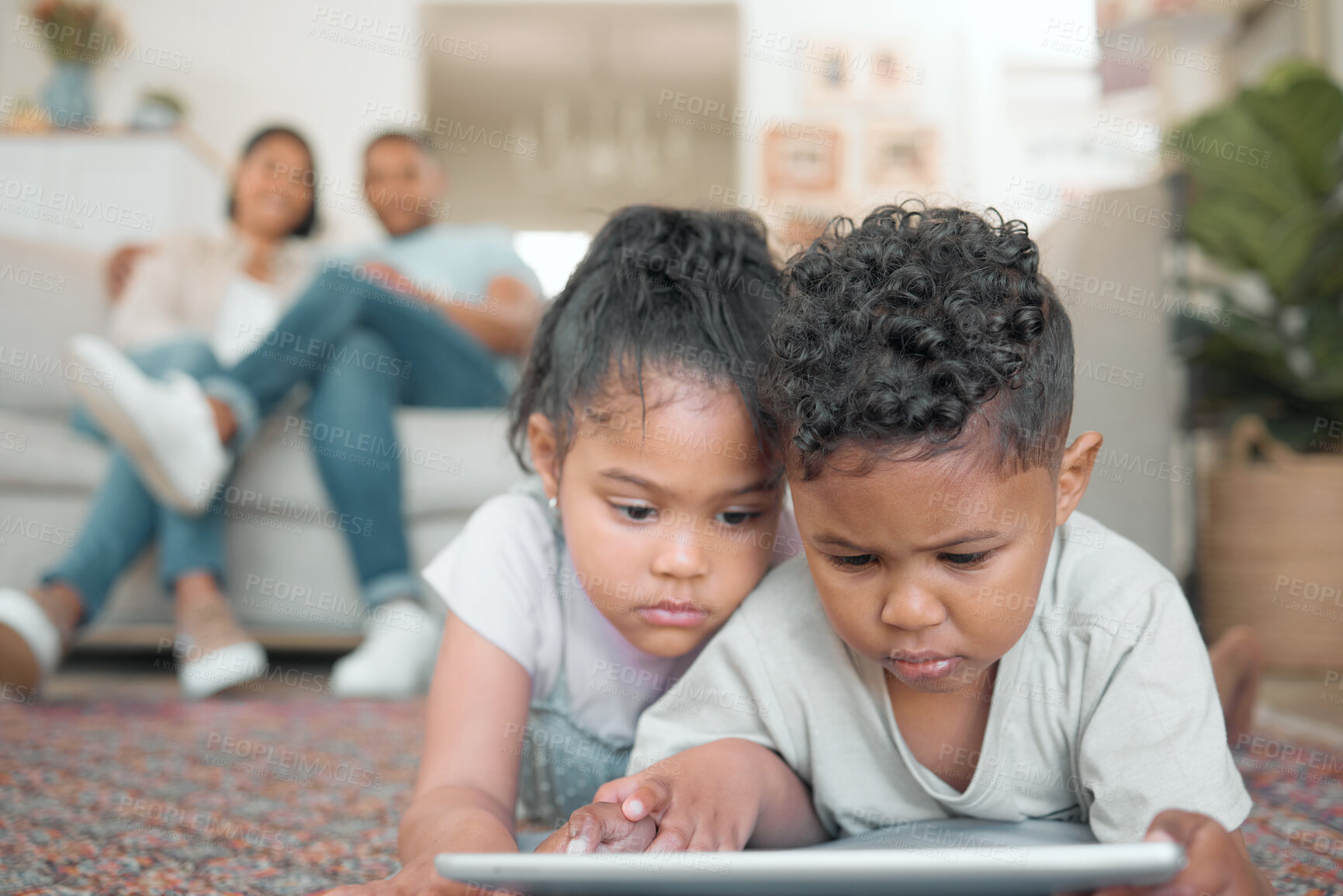 Buy stock photo Shot of two young children lying on the floor in the living room and using a digital tablet