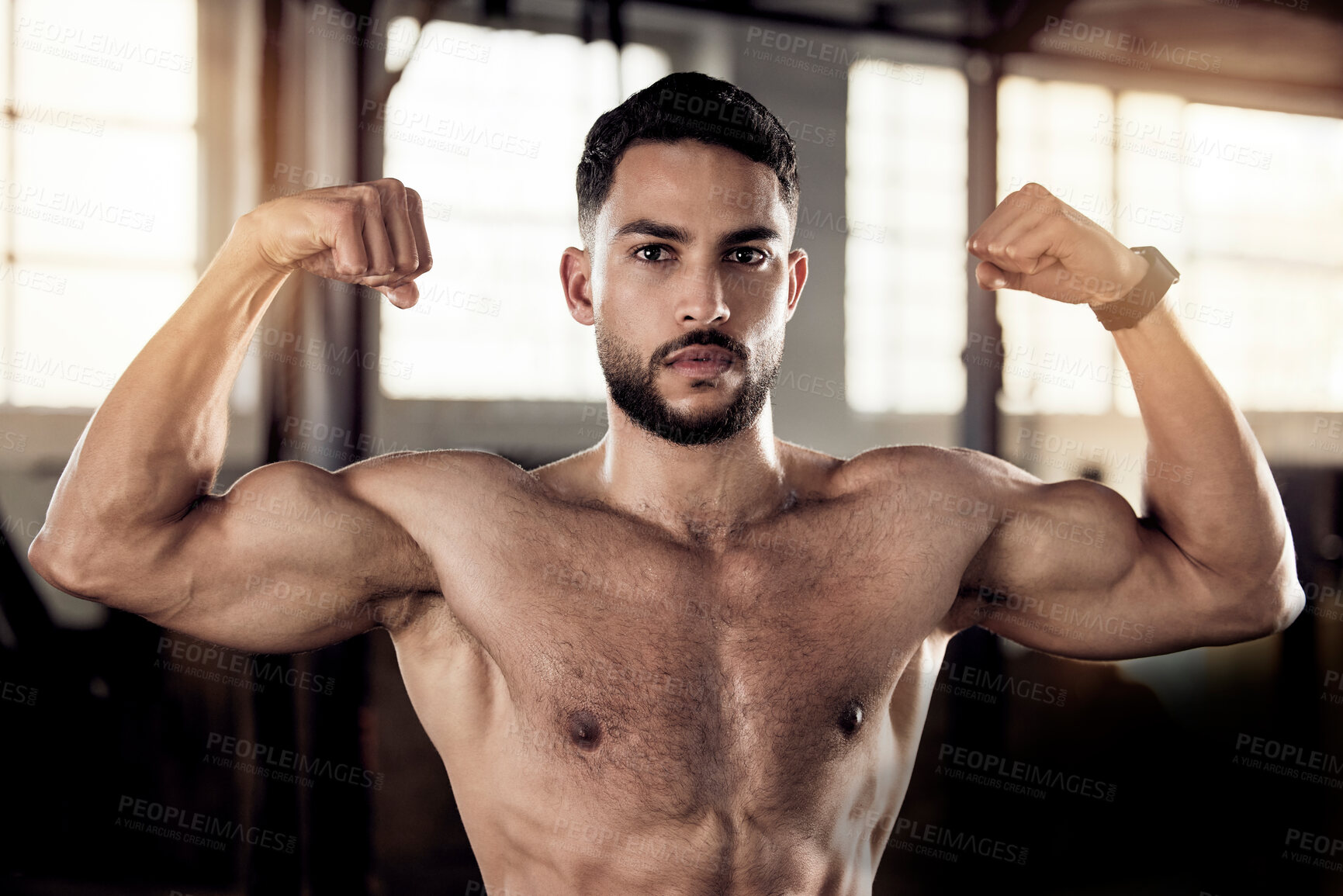 Buy stock photo Shot of a young man flexing his muscle in a gym