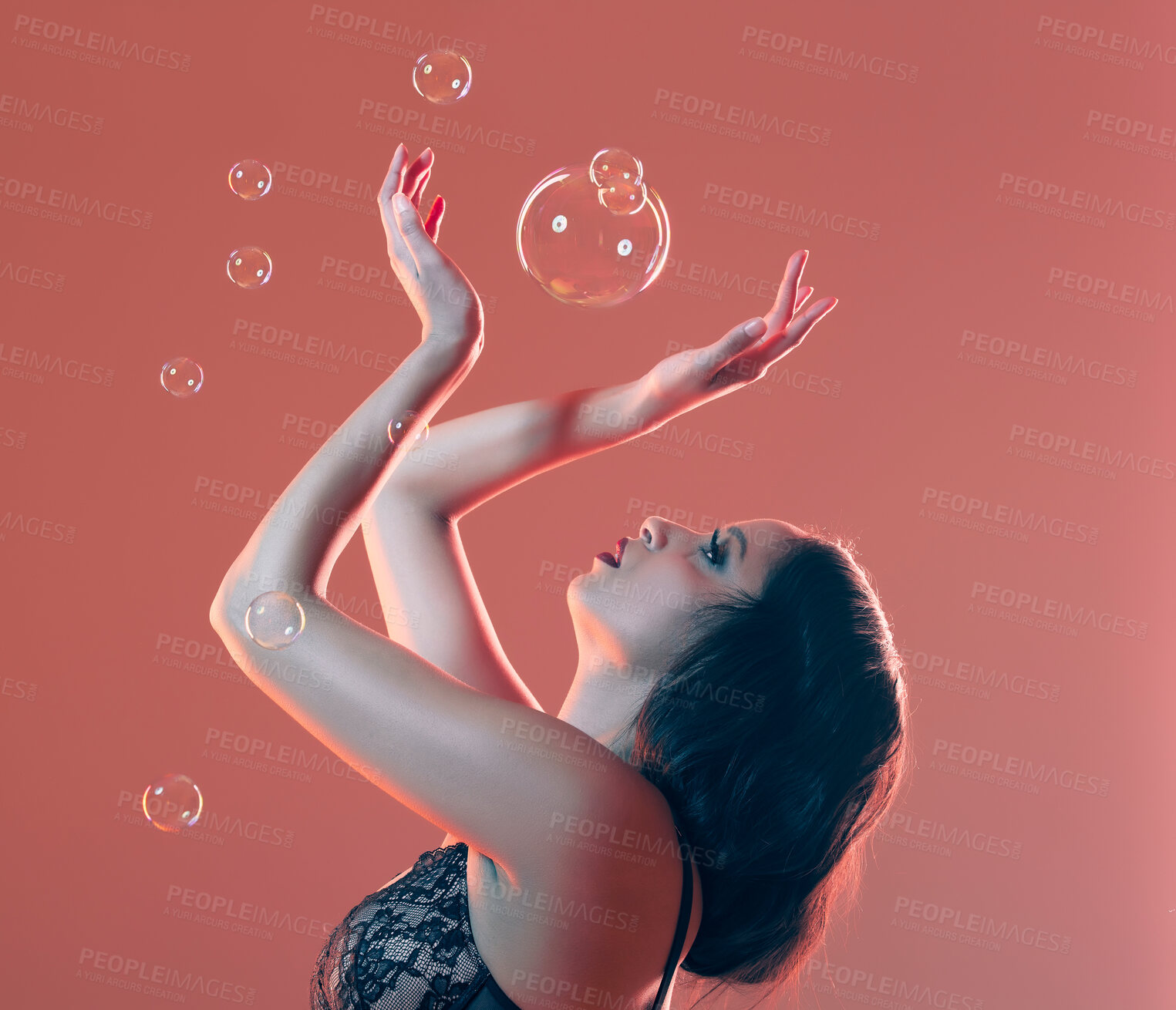 Buy stock photo Cropped shot of a beautiful young woman posing in studio surrounded by bubbles against a red background