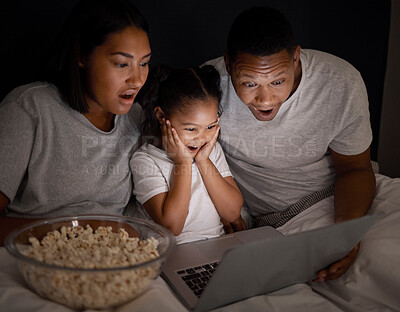 Buy stock photo Shot of a young couple sitting in bed with their daughter and using a laptop at night