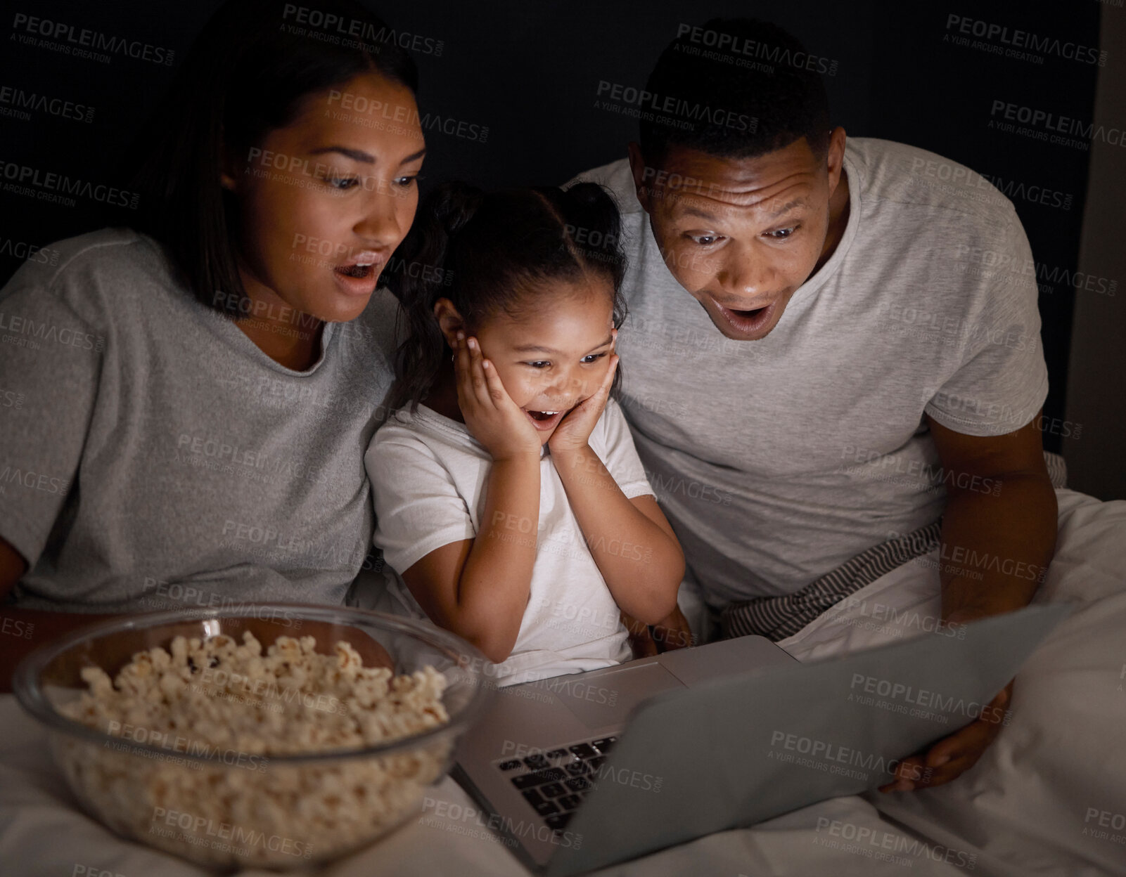 Buy stock photo Shot of a young couple sitting in bed with their daughter and using a laptop at night