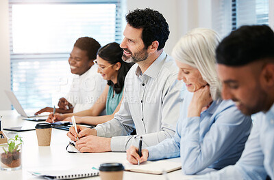 Buy stock photo Shot of a mature businessman writing notes while attending a meeting with his colleagues in an office