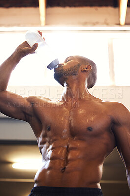 Buy stock photo Low angle shot of a muscular young man drinking water while exercising in a gym