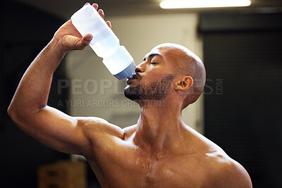 Buy stock photo Shot of a muscular young man drinking water while exercising in a gym