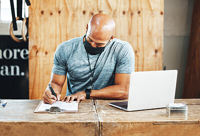 Buy stock photo Shot of a muscular young man wearing a face mask and writing notes while working in a gym