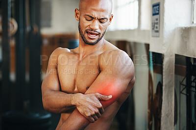 Buy stock photo Shot of a muscular young man holding his arm in pain while exercising in a gym
