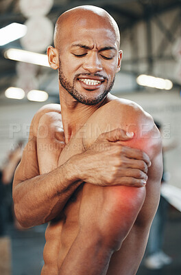 Buy stock photo Shot of a muscular young man holding his arm in pain while exercising in a gym