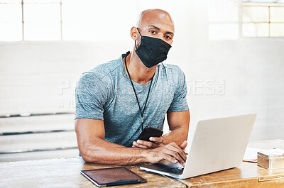 Buy stock photo Portrait of a muscular young man wearing a face mask and using a laptop while working in a gym
